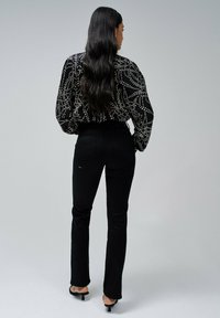 Blusa negra con estampado y un diseño fluido, combinada con jeans negros ajustados. El look se completa con unos zapatos de tacón negro delgado.