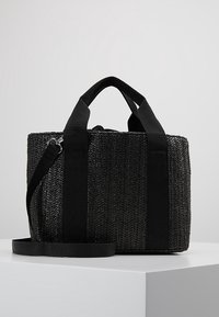Bolso tote tejido negro con asas de tela negra gruesa y correa desmontable. Presenta una superficie texturizada con un patrón de espiga repetido.