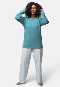 Turquoise lange mouw top van textuurstof, gecombineerd met losse gestreepte pyjamabroek in lichtblauw en wit. Zacht, comfortabel ontwerp.