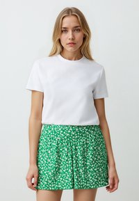 T-shirt bianco in cotone abbinato a una gonna verde con un piccolo motivo floreale bianco, design a pieghe e vita elastica.