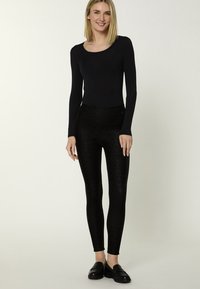 Black long-sleeve top paired with high-waisted black leggings featuring a subtle leopard print. The outfit is completed with black loafers.