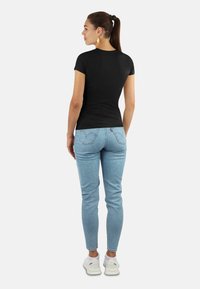 Schwarzes Kurzarm-T-Shirt, Slim Fit, kombiniert mit hellblauen Skinny-Jeans, die rückwärtige Taschen und ein kleines Logo-Detail aufweisen. Weiße Sneakers.