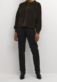 Maglione a righe marroni e nere con scollatura rotonda e spalle cadenti, abbinato a pantaloni neri aderenti e stivali alla caviglia.