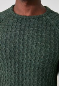 Groen gebreide trui met een gestructureerd kabelpatroon, een ronde halslijn en raglanmouwen. De stof lijkt zacht en dik.