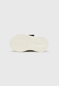 Sola de borracha branca de um ténis preto com padrão de piso, vista de baixo contra um fundo branco liso.