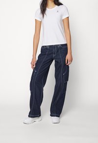 Hvid T-shirt med et lille sort logo, parret med løstsiddende mørkeblå cargo jeans med kontraststing og sidelommer.