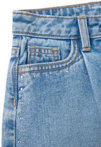 Light blue denim jeans with a high waist, featuring decorative silver studs along the side seam and contrasting stitching details.