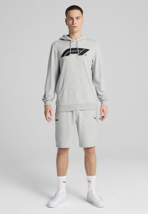 Grå hættetrøje med sort logo, parret med grå shorts, hvide sokker og hvide sneakers. Afslappet atletisk sæt med en løs pasform.
