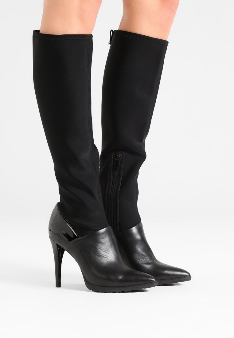 Botas negras hasta la rodilla con caña de tela ajustada, puntera y tacón de charol brillante, punta afilada y cierre de cremallera lateral.