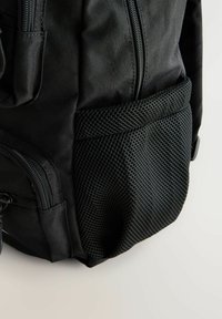 Schwarzer Rucksack aus strukturiertem Stoff mit einem Netz-Seitentasche und Reißverschlussfächern für sichere Aufbewahrung.