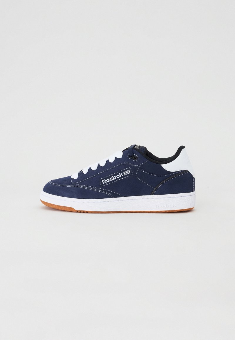 Baskets Reebok bleu marine et blanc avec lacets blancs et semelle en gomme, vue latérale montrant le logo et les coutures détaillées.