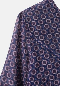 Modrá vzorovaná látka s květinovými motivy v růžové a krémové barvě, s texturovaným povrchem a diagonálním švem.