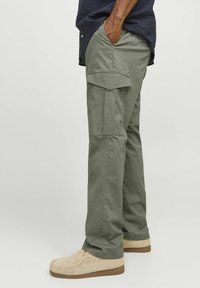 Olivgrüne Cargo-Hosen mit mehreren Taschen, gerade geschnitten, aus Baumwollmaterial, kombiniert mit hellbraunen Wildlederschuhen. Flacher Vorderteil-Design.