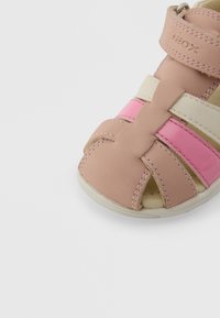 Ροζ σανδάλι για παιδάκι με μπεζ και φωτεινό ροζ λουράκια, κλείσιμο με βέλκρο και λευκή λαστιχένια σόλα σε λευκό φόντο.
