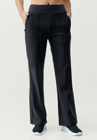 Juodos, aukštai juosmeninės sportinės kelnės su lygiu paviršiumi, tiesiomis kojomis, šoninėmis kišenėmis ir siuvinėjimo detalėmis. Dėvimos su juodais sportbačiais.