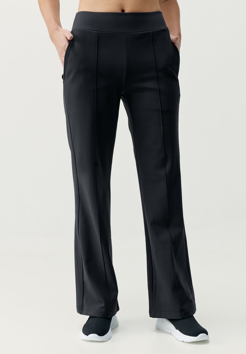 Juodos, aukštai juosmeninės sportinės kelnės su lygiu paviršiumi, tiesiomis kojomis, šoninėmis kišenėmis ir siuvinėjimo detalėmis. Dėvimos su juodais sportbačiais.