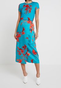 Vestido turquesa con mangas cortas, que presenta un estampado floral en rojo. Largo hasta la rodilla con un detalle de cinturón y una textura suave.