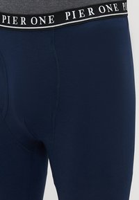 Ναυτικό μπλε κολάν με μαύρη μέση που έχει λευκό κείμενο "PIER ONE". Λείος υφή, λυγισμένος σχεδιασμός με λεπτομέρειες ραφής.