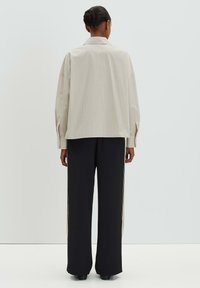 Light striped button-up shirt with a relaxed fit, paired with loose black trousers featuring side accents. Fabric appears smooth and lightweight.