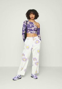 Top crop de manga longa em camuflagem roxa combinado com calças brancas com grandes padrões florais em lavanda. O modelo usa ténis roxos e pretos.