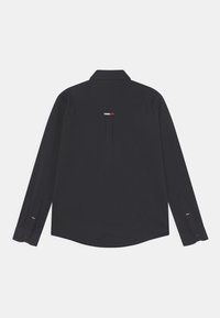 Camicetta a maniche lunghe blu navy con colletto a camicia, dotata di uno spacco sul retro e di un piccolo accento tricolore vicino al collo. Tessuto di texture liscia.