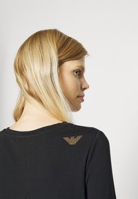 Zwarte shirt met een ronde halslijn, met een gouden strass accent in een driehoekig ontwerp op de bovenrug. Zachte stof.