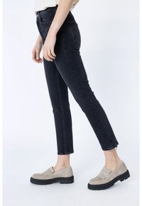 Jeans skinny de mezclilla oscura con cintura alta y dobladillo deshilachado, combinados con unos zapatos slip-on de color beige claro que cuentan con flecos y suelas gruesas.