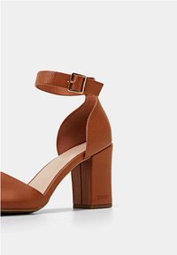 Sandale à talons hauts en faux cuir marron avec une sangle à la cheville, finition texturée, bout carré et talon bloc arborant le logo de la marque.