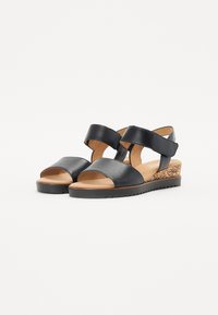 Black leather wedge sandals with an open toe, two strap design, and textured cork accent on the wedge heel. Smooth inner lining.