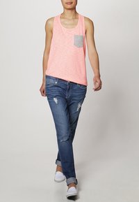 Ljust rosa linne med en grå ficka, matchat med slitna blå jeans och vita slip-on skor. Avslappnad passform; mjuk textur.