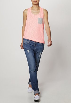 Helles rosa Tanktop mit einer grauen aufgesetzten Tasche, kombiniert mit zerrissenen blauen Jeans und weißen Slippern. Lässiger Schnitt; weicher Stoff.