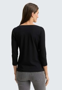 Black long-sleeve top with a boat neckline, featuring a smooth texture and fitted design. Paired with grey, form-fitting pants.