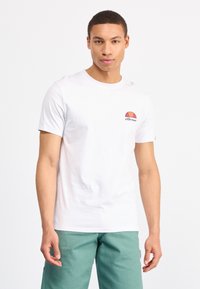 Weißes T-Shirt mit kurzen Ärmeln und rundem Halsausschnitt, mit einem bunten Logo auf der linken Brust. Modell trägt mintgrüne Hose. Flache Textur.