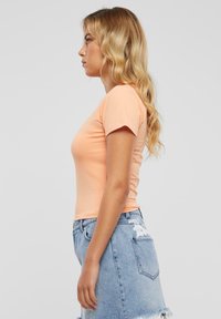 Ferskenfarget tettsittende t-skjorte med korte ermer, kombinert med et lyseblått denimskjørt med frynset kant og broderte detaljer.