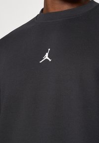 Schwarzer Baumwollpullover mit Rundhalsausschnitt, der ein kleines weißes Jumpman-Logo auf der Brust und einen weichen, strukturierten Stoff aufweist.