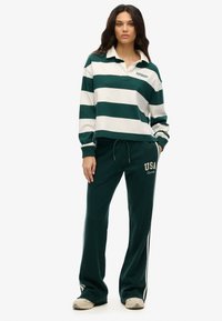 Groen en wit gestreepte rugbystijl pullover met een kraag en geborduurd logo, gecombineerd met groene sweatpants met 'USA' opdruk.