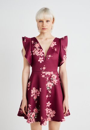 Burgunderfarget kjole med blomstermønster i rosa, V-hals, korte volangermer, tettsittende midje og utsvingt skjørt, laget av glatt stoff.