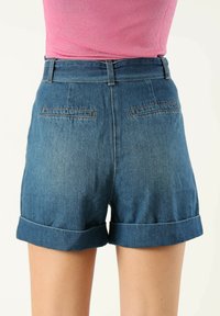 Shorts de mezclilla en azul oscuro, con una vuelta en el dobladillo, bolsillos traseros y una cintura ajustada. Material: tejido suave y ligeramente texturizado.
