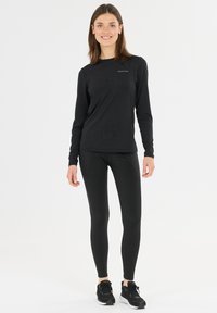 Svart långärmad träningströja med logotyp, ihop med åtsittande svarta leggings och svarta träningsskor, på en enfärgad vit bakgrund.