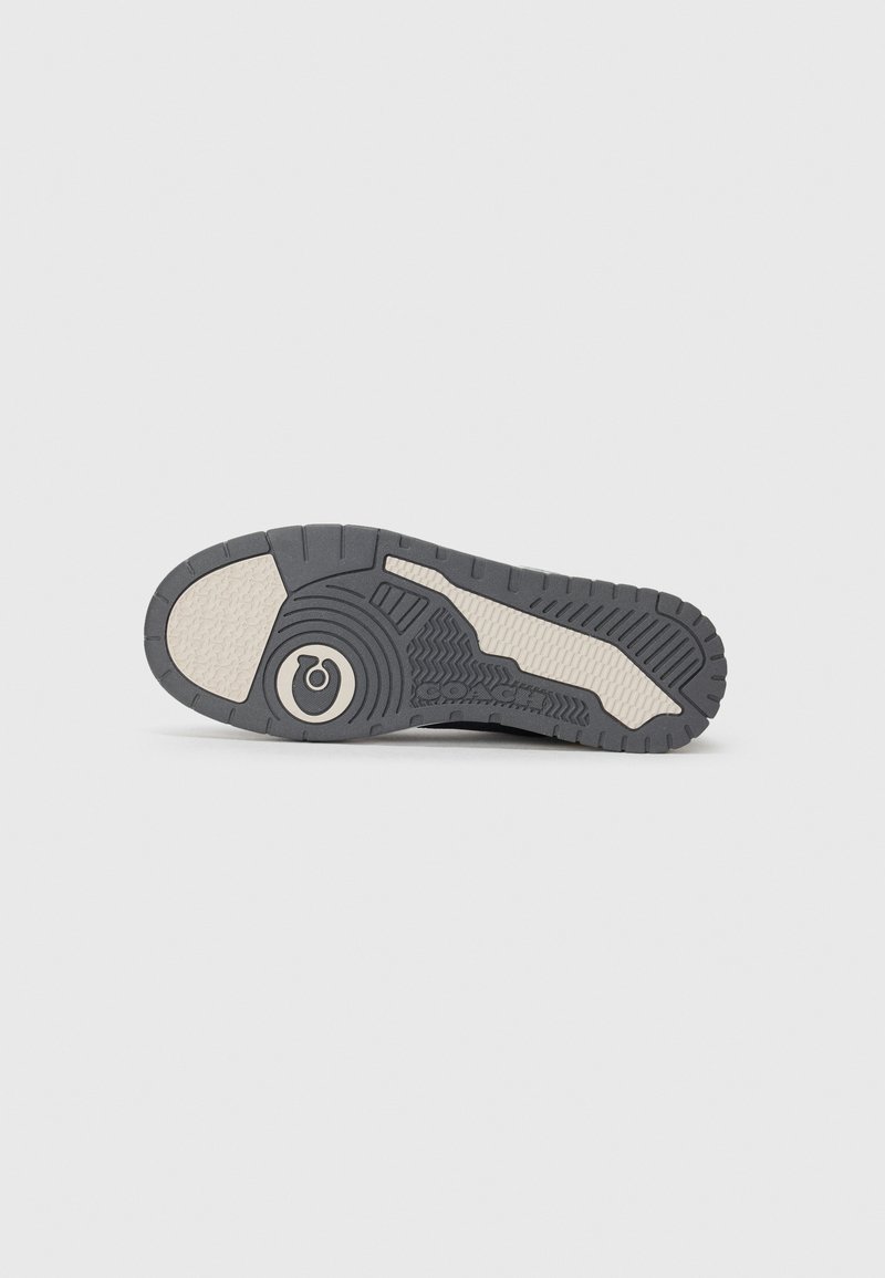 Gray rubber shoe sole with textured patterns, including alternating smooth and ridged sections. Features a circular emblem in the center.