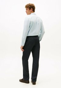 Lys blå skjorte med lange ærmer, parret med mørk navy bukser, iført brune loafers, set bagfra.