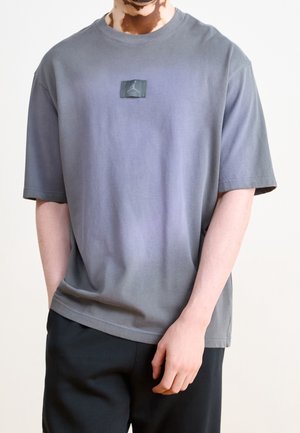 Grå gradient t-shirt med korte ærmer, har et patch-logo på brystet. Blødt bomuldsmateriale, afslappet pasform og crew neck-design.