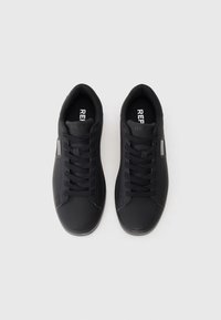 Une paire de baskets basses noires avec des lacets noirs et un logo "REPLAY" blanc sur la languette et la semelle intérieure, présentée de dessus sur un fond blanc.
