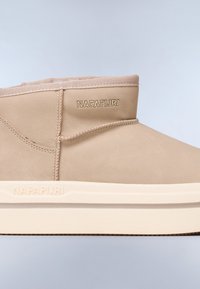 Stivale alla caviglia in suede beige con suola bianca testurizzata, caratterizzato da un design cucito e un marchio in rilievo sul lato. Collo in tessuto liscio.