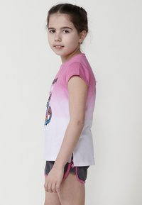 Camiseta de manga corta en ombré rosa y blanco con un diseño impreso colorido. Combinada con pantalones cortos grises con ribetes rosas y acentos de estrellas.