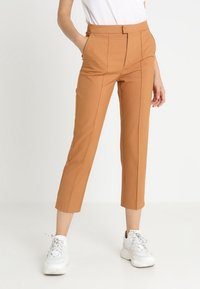 Tan tailored trousers with a straight cut, featuring front pockets, pressed seams, and a smooth texture. Worn with white sneakers.
