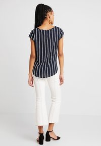 Blusa a righe navy con scollatura rotonda, maniche corte e orlo curvo, abbinata a pantaloni bianchi svasati e scarpe con tacco nere.