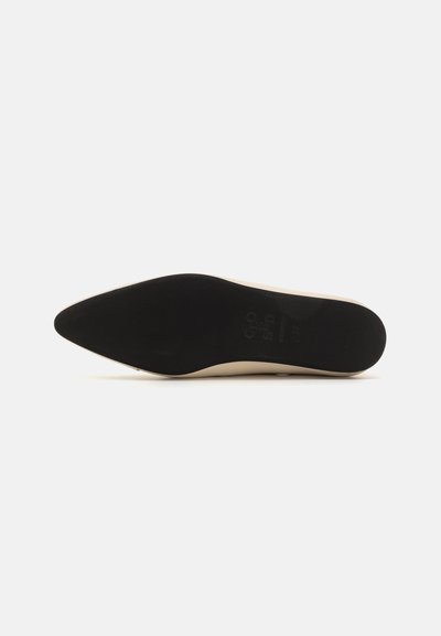 Pointed-toe shoe with a smooth beige upper and a textured black sole. Features a sleek design and minimal hardware, focusing on simplicity.