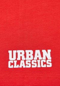 Raudona medvilninė marškinė su lygiu tekstūra ir dideliu baltu "URBAN CLASSICS" spaudiniu centre ant priekio, parašytu drąsiais, stačiakampiais raidėmis.