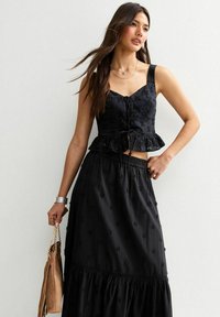 Top peplum nera con ricami floreali e legature frontali, abbinato a una gonna lunga a strati con vestibilità ampia e vita elastica.